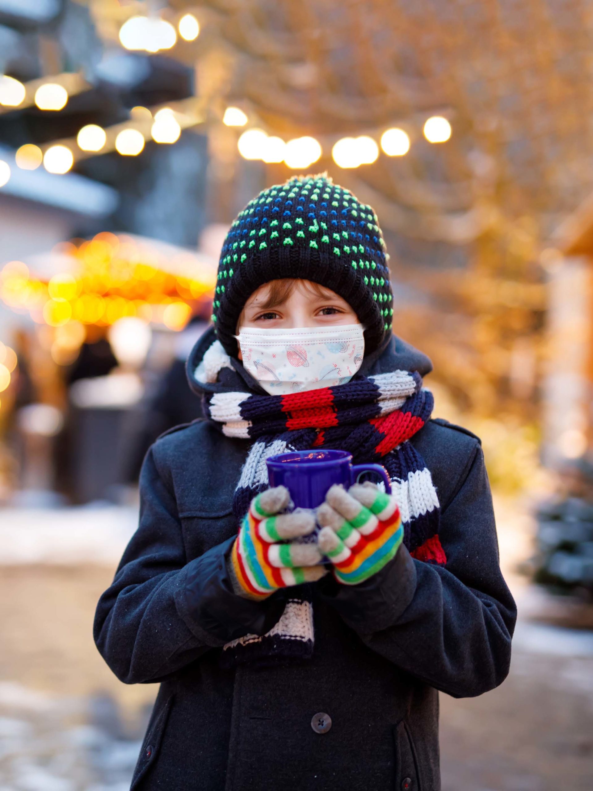 boy holding mug smiles with mask on in the cold weather outside