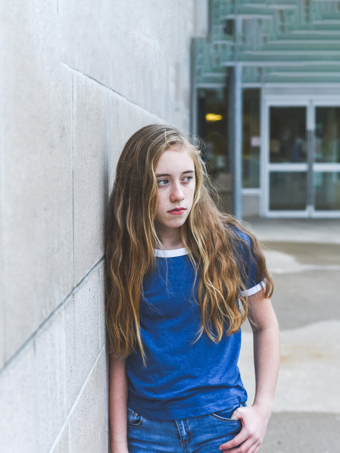 teen leans against a wall and looks off into the distance