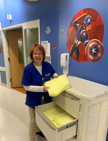 CHOC volunteer Debbie smiles while organizing yellow gowns in a hospital hallway